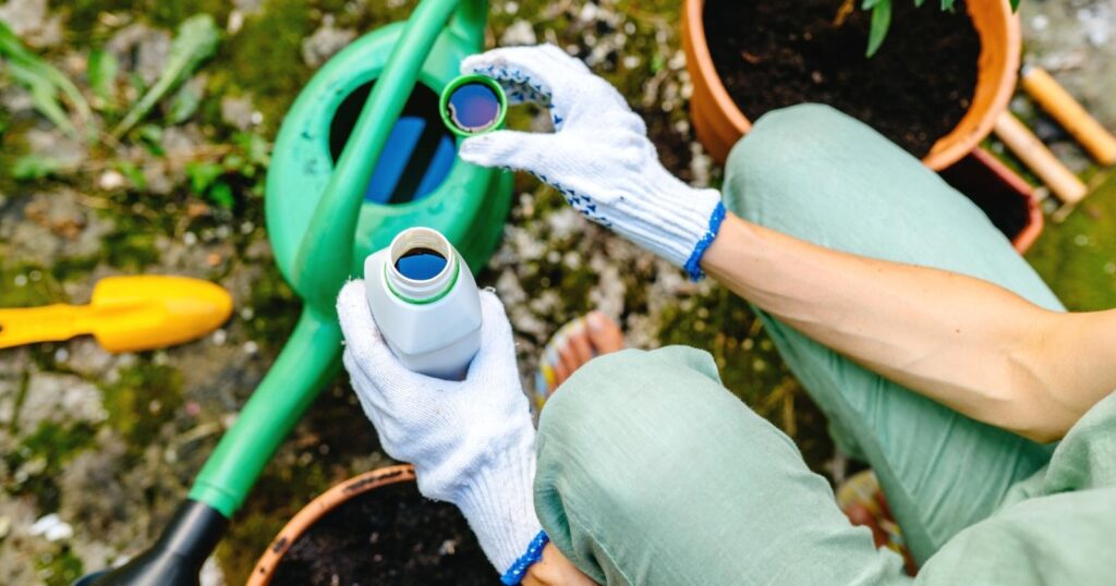Two gloved hands mixing green fertilizer into a green watering bucket.